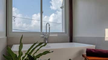 A modern bathroom with a large window, a freestanding bathtub, and a wooden stool.