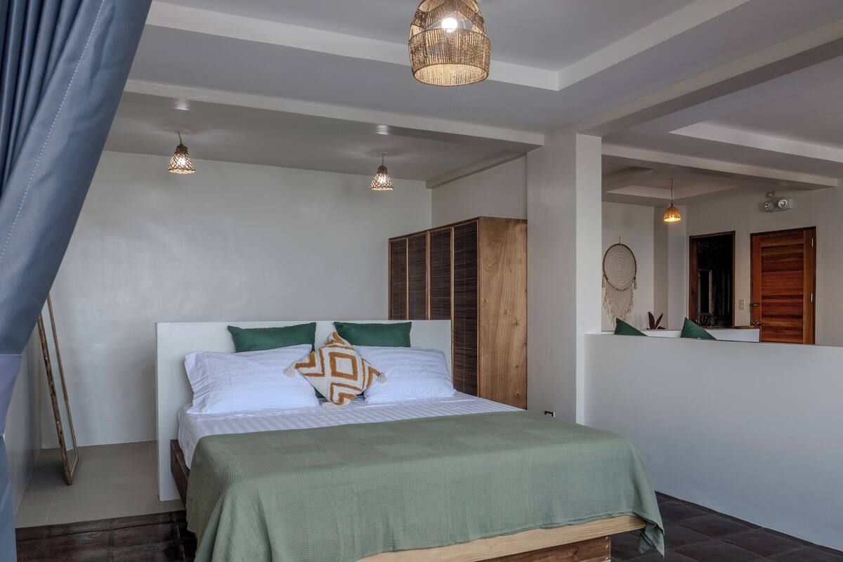 A bedroom with a bed, green pillows, a wooden wardrobe, and a mirror.