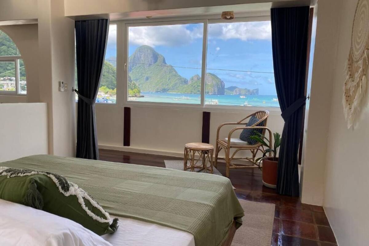 A bedroom with a bed, a chair, a small table, and a view of the ocean and mountains.