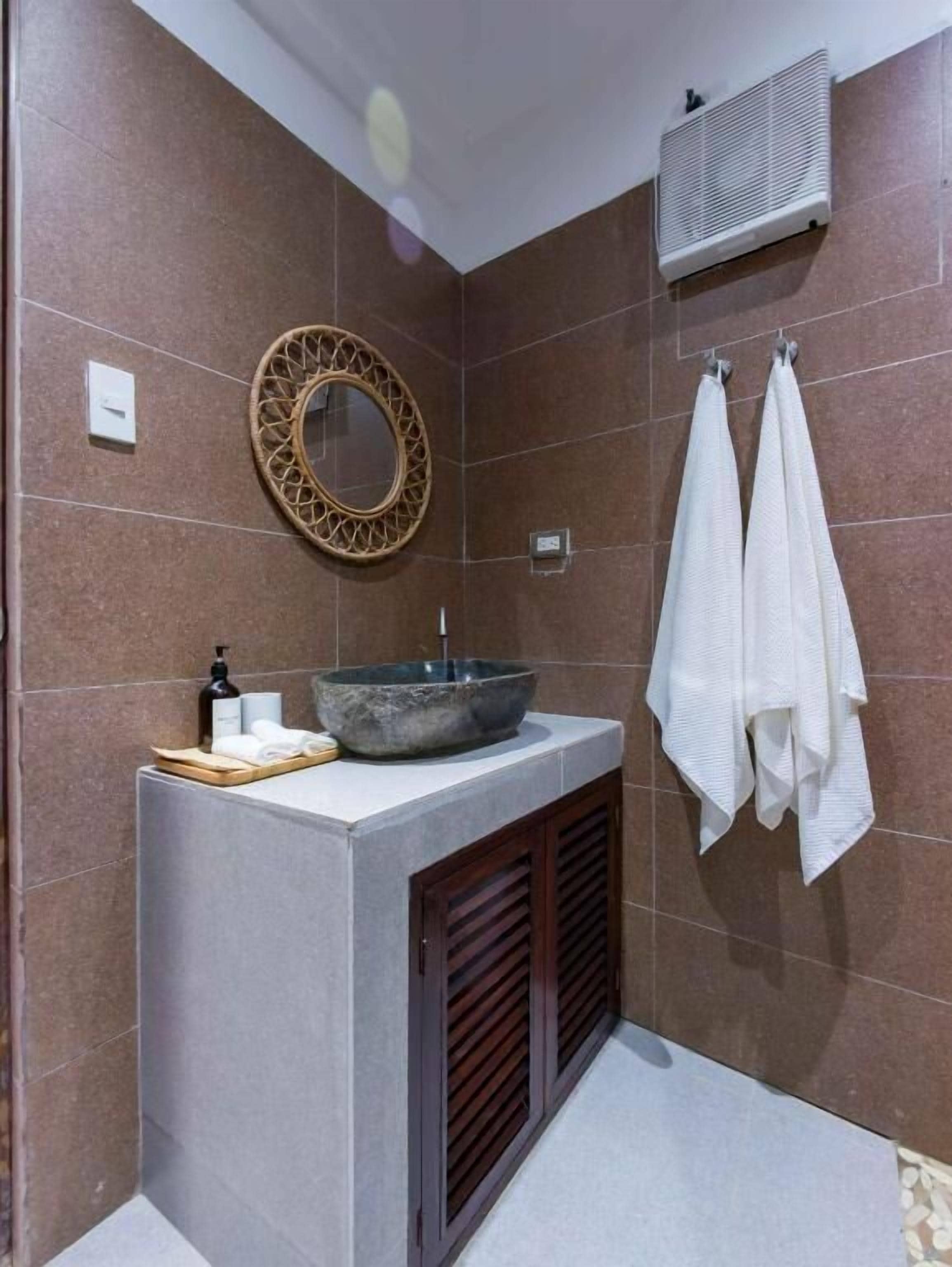 Un bany amb un rentapeus de pedra, un mirall rodó, dues tovalloles i una unitat de ventilació.