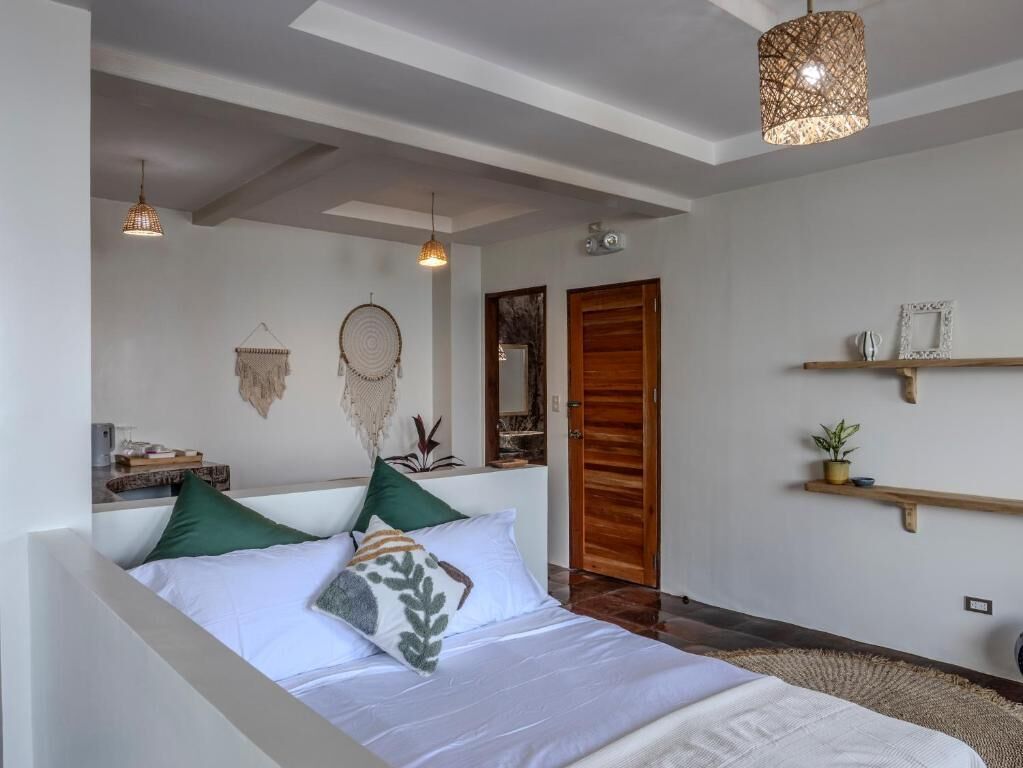 A bedroom with a bed, bedside tables, a wooden door, and a hanging light fixture.
