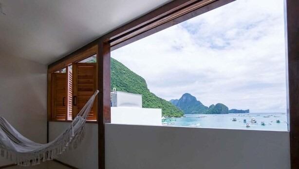 Quarto com rede, vista para o mar e varanda de madeira.