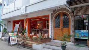 Restaurante com mesas ao ar livre, porta de madeira e quadro de cardápio.