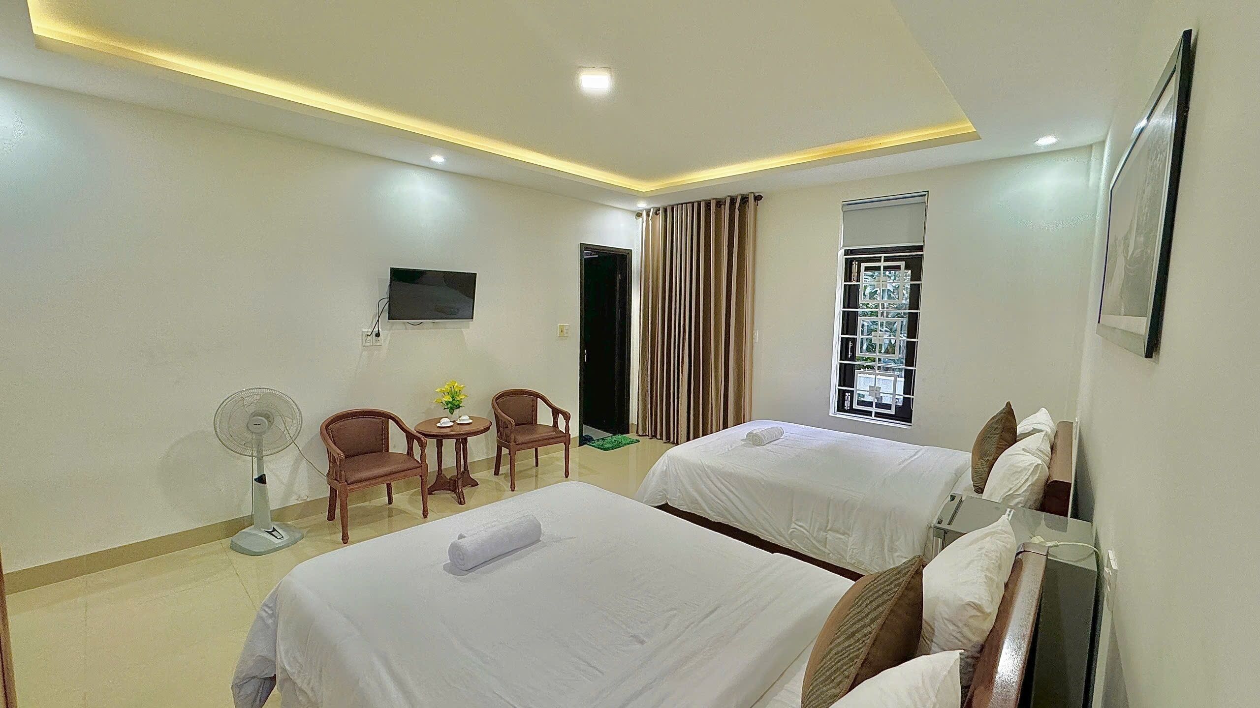 A hotel room with two beds, a TV, a fan, and a window with curtains.