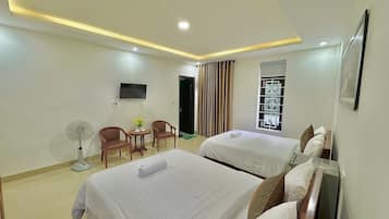 A hotel room with two beds, a TV, a fan, and a window with curtains.