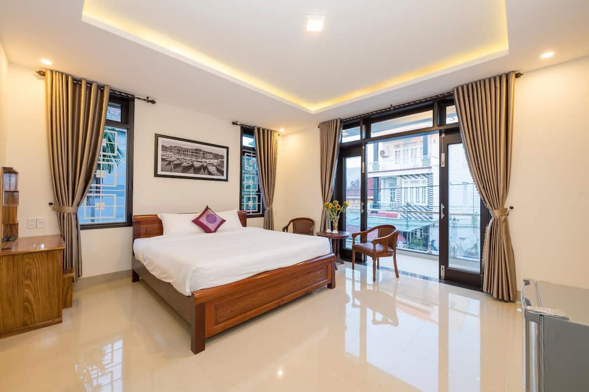 A modern hotel room with a large bed, a desk, and a balcony with a view of the city.