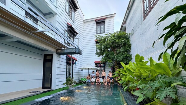 Une cour avec une piscine, entourée de bâtiments et d’une végétation luxuriante.