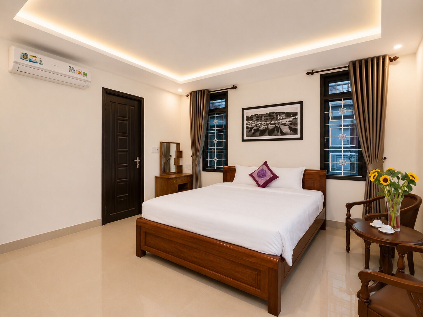 A hotel room with a wooden bed, a bedside table, a chair, a desk, and a window with curtains.