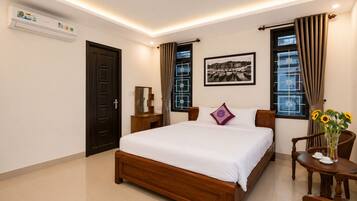 A hotel room with a wooden bed, a bedside table, a chair, a desk, and a window with curtains.