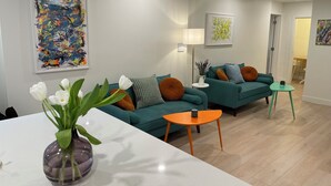 Ein modernes Wohnzimmer mit türkisfarbenen Sofas, einem weißen Couchtisch und einer violetten Vase mit weißen Blumen.
