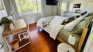 A bedroom with a bed, a bedside table with a lamp, a mirror, a television, and a window with curtains.