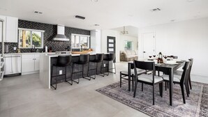 Una cocina moderna con una isla central, taburetes de bar y una zona de comedor con una mesa preparada para cuatro.