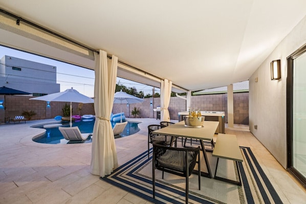 A covered patio with a pool, outdoor seating, and a table with a beverage bucket.