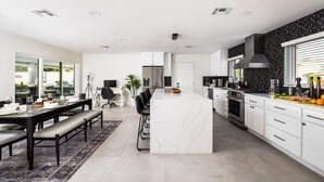 Una cocina moderna con armarios blancos, una isla de mármol y un respaldo negro.