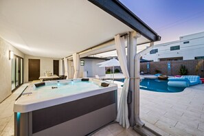 A hot tub with a view of a swimming pool and a modern building in the background.