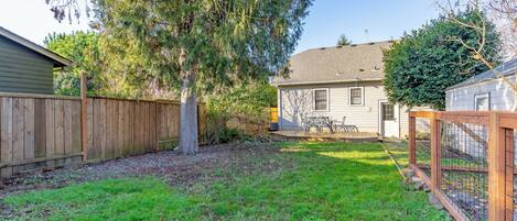 A backyard with a wooden fence, a tree, and a house.