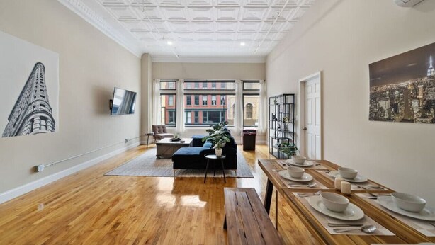 A spacious living room with a wooden floor, a black sofa, a coffee table, and a dining area set with white plates and bowls.