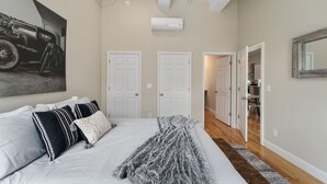 A bedroom with a large bed, two white doors, a hallway, and a mounted air conditioner.