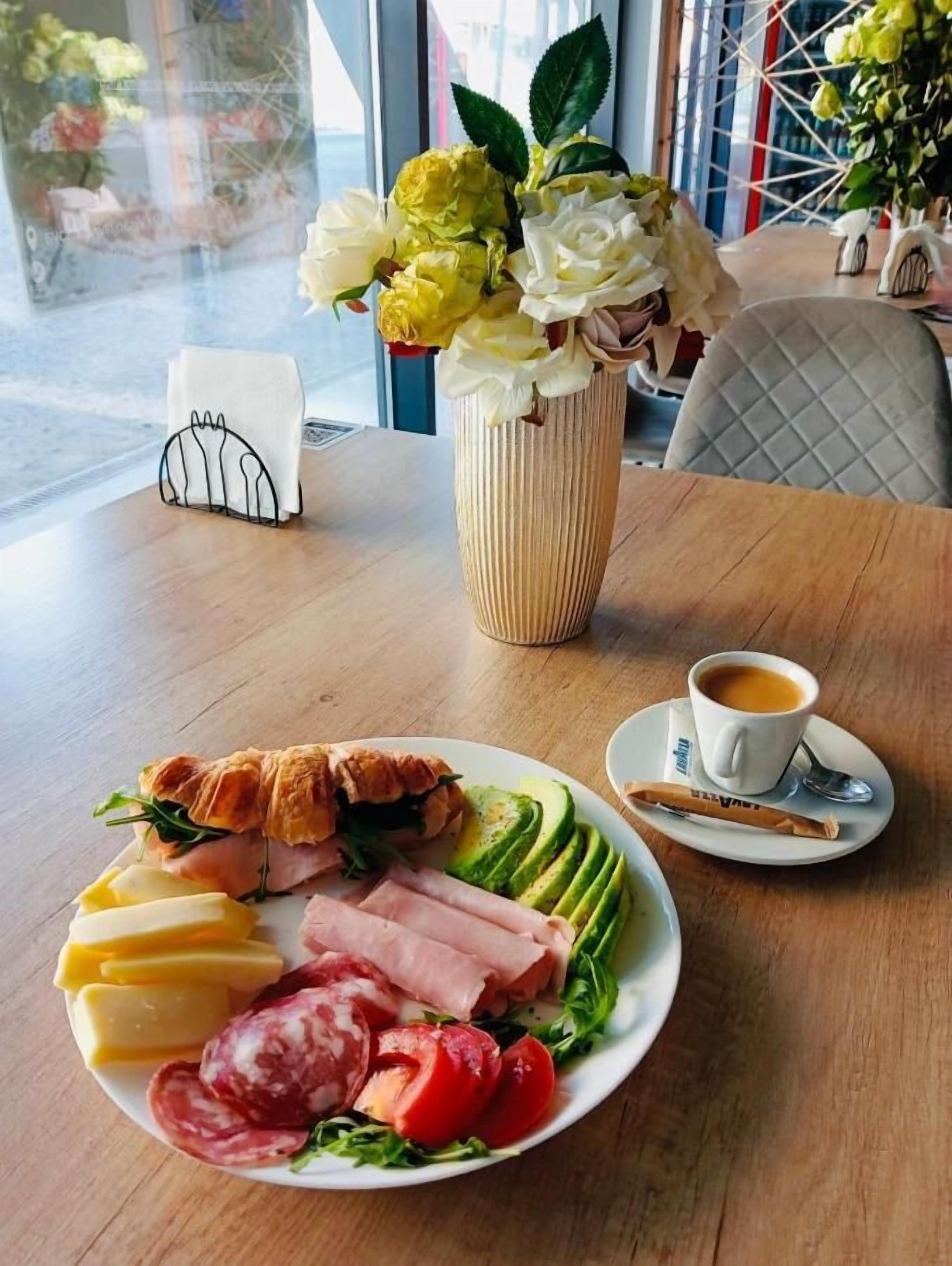 A table with a plate of food, a cup of coffee, and a vase of flowers.