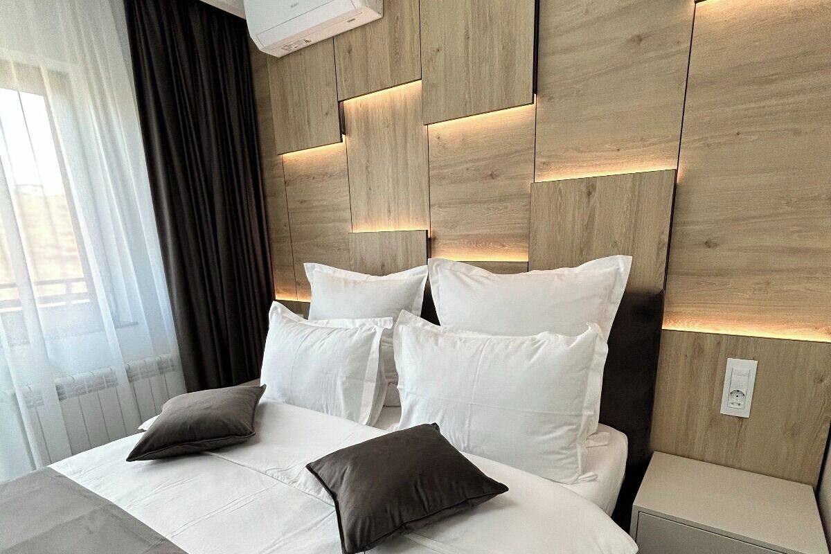 A modern hotel room with a large bed, white bedding, and a wooden headboard with integrated lighting.
