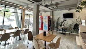 Un comedor moderno con mesas y sillas, una máquina expendedora y un mural en la pared.