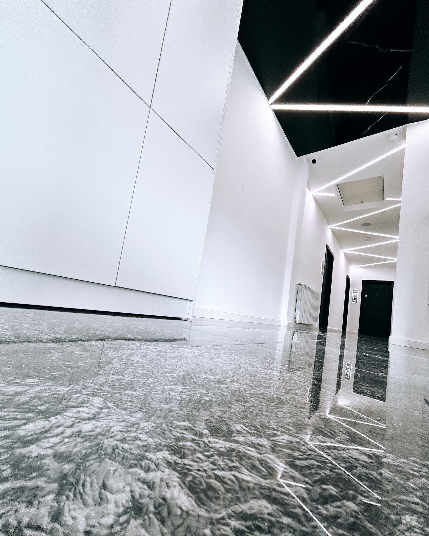 Un interior moderno con un suelo de mármol reflectante, diseño geométrico en el techo y una estética limpia y minimalista.