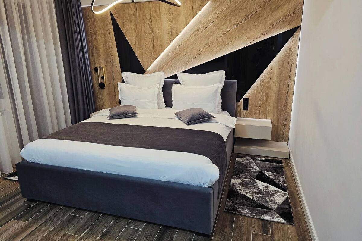 A modern bedroom with a bed, bedside tables, and a unique geometric wall design.