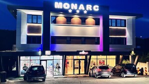 Un edificio moderno con un letrero 'MONARC', que cuenta con una entrada amplia y varios coches estacionados frente a él.