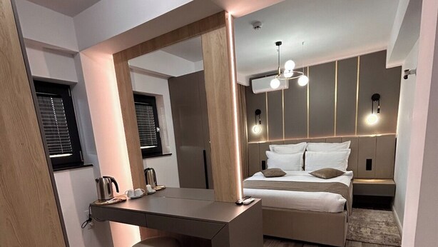 Un dormitorio moderno con cama, mesitas de noche, escritorio y un espejo grande.