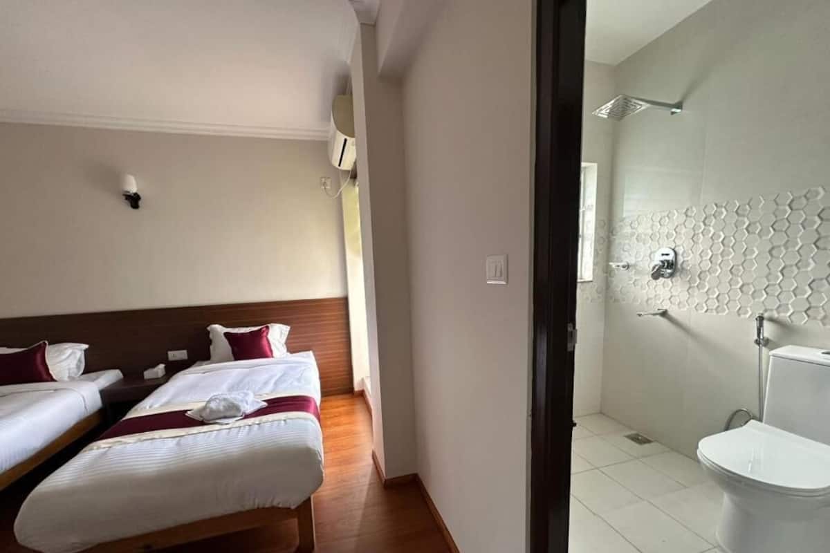 A hotel room with two beds, a bathroom with a modern shower, and a toilet.