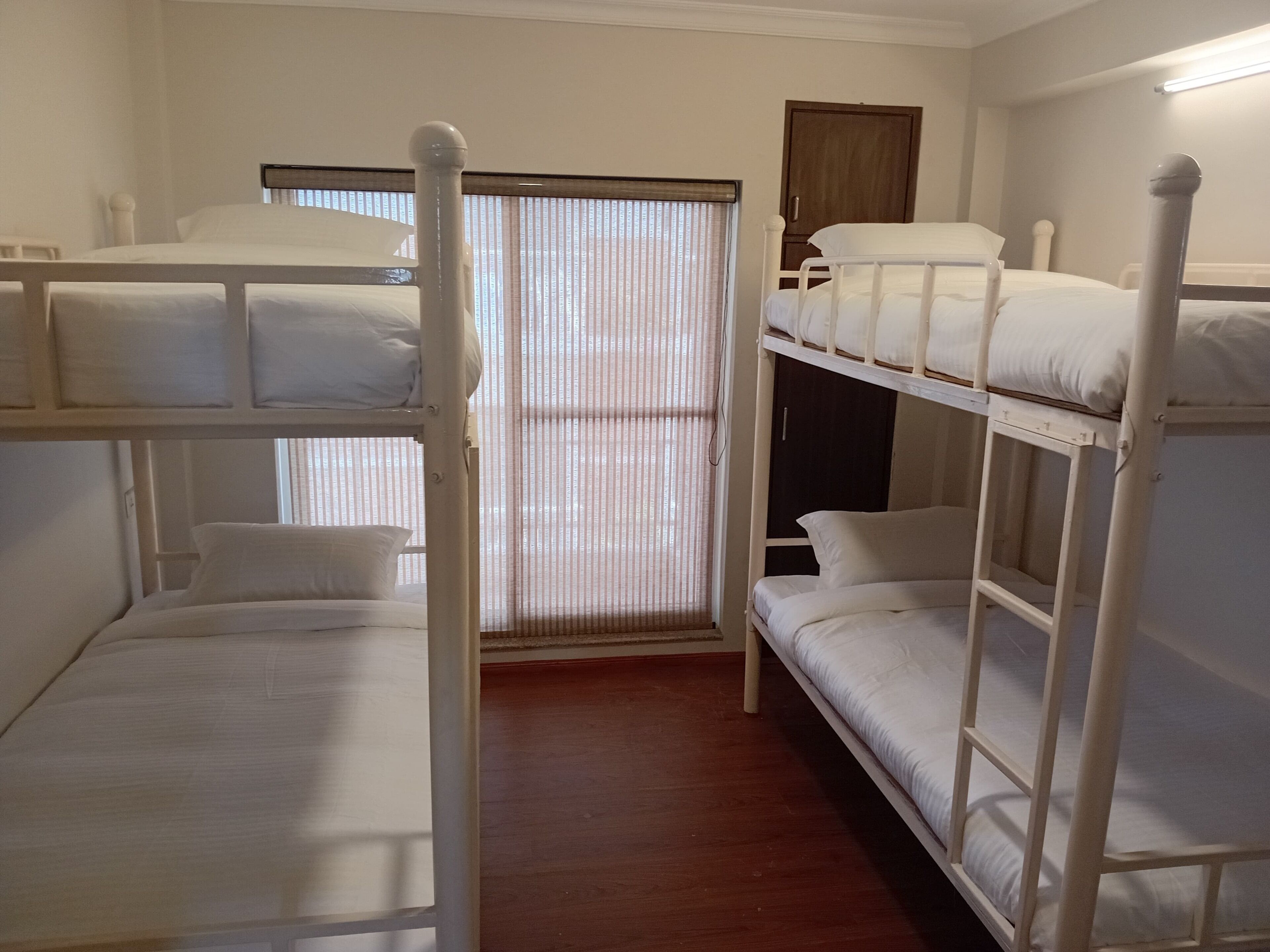 A bunk bed room with a wooden floor, a window with blinds, and a door.