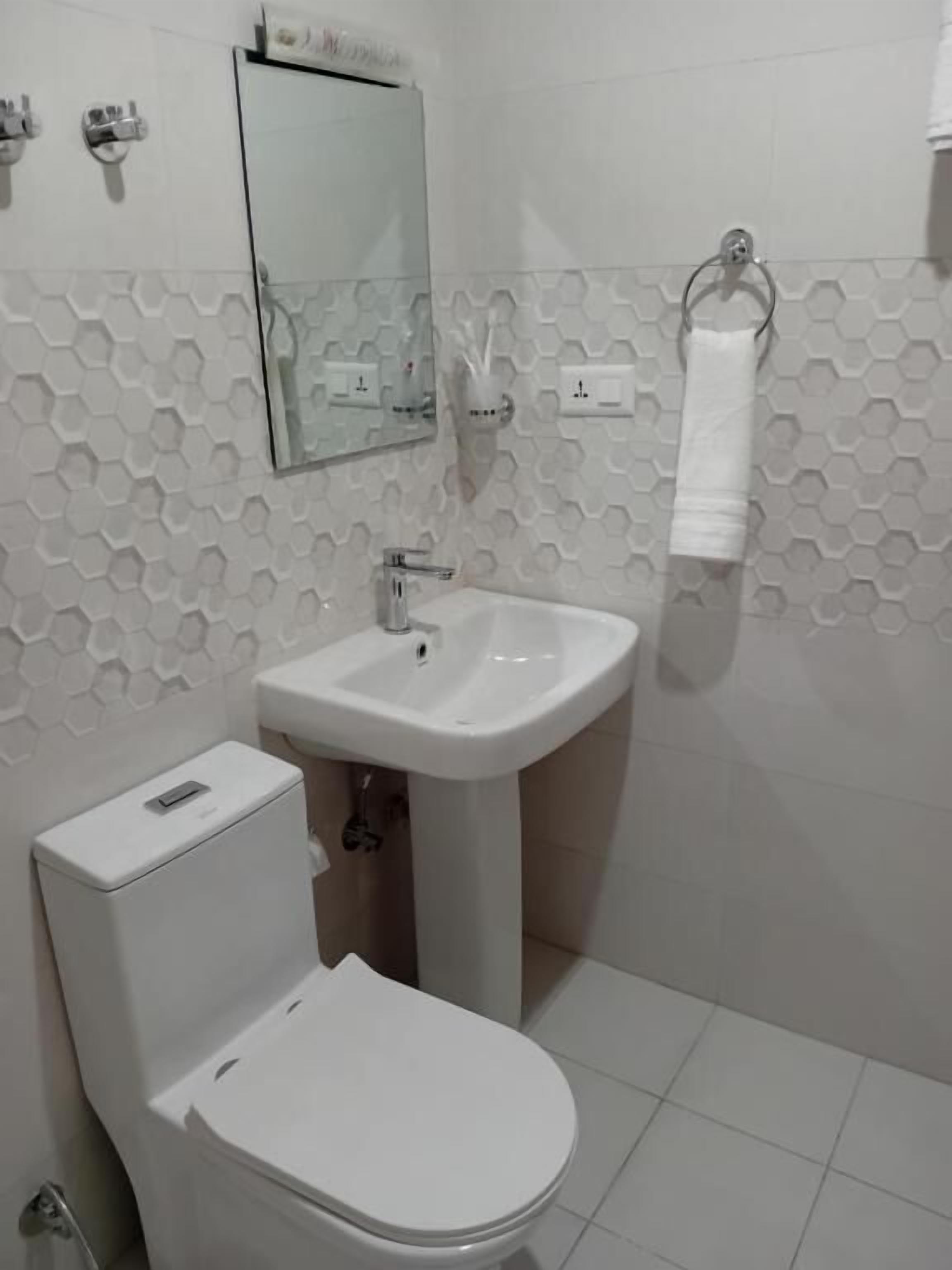Une salle de bain avec des toilettes blanches, un lavabo sur colonne et un miroir au-dessus du lavabo.