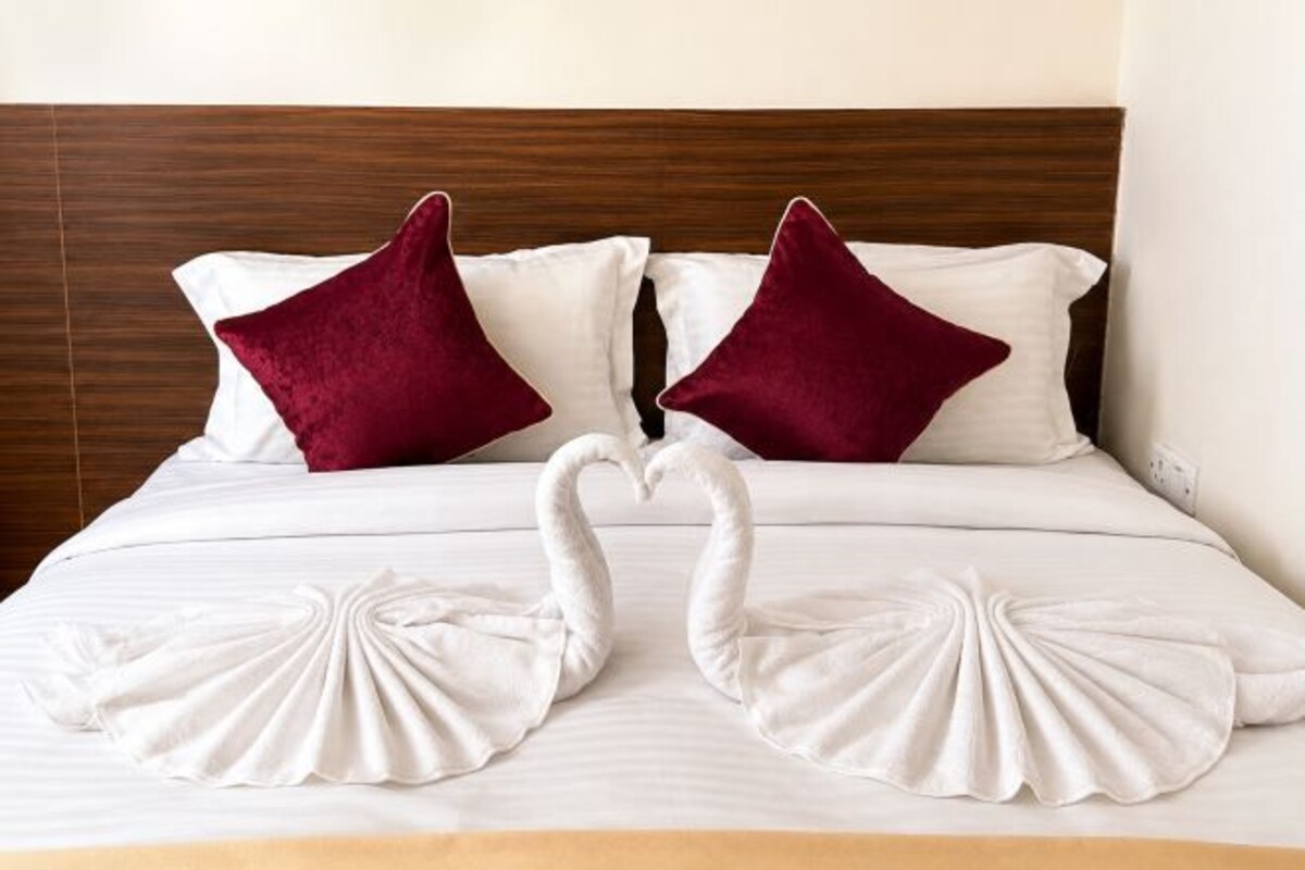 A bed with white bedding, two red pillows, and two swan-shaped beddings.