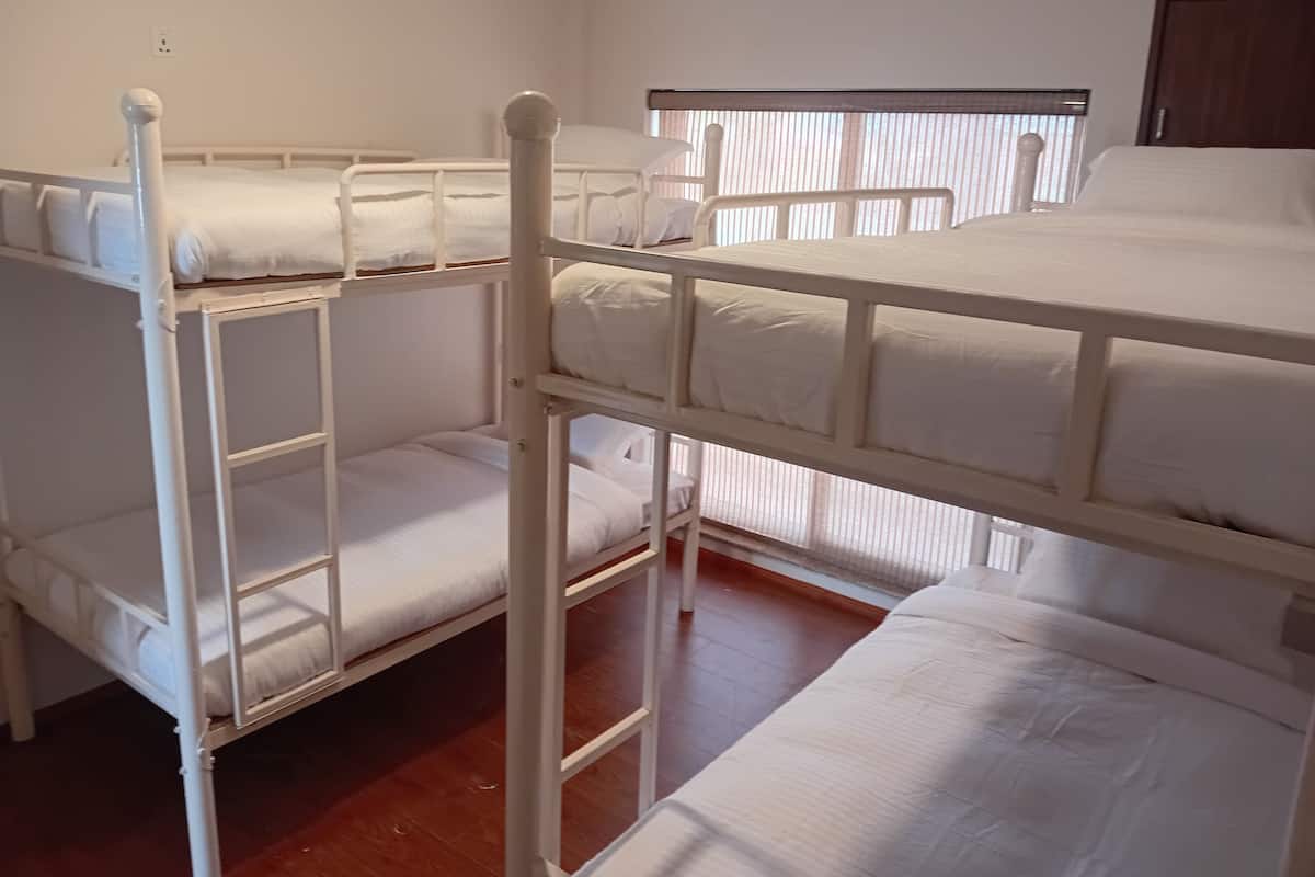 A bunk bed room with white bedding and a window with blinds.