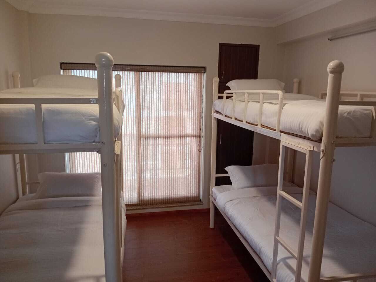 Una habitació amb llits superposats, una finestra amb persianes i una porta.