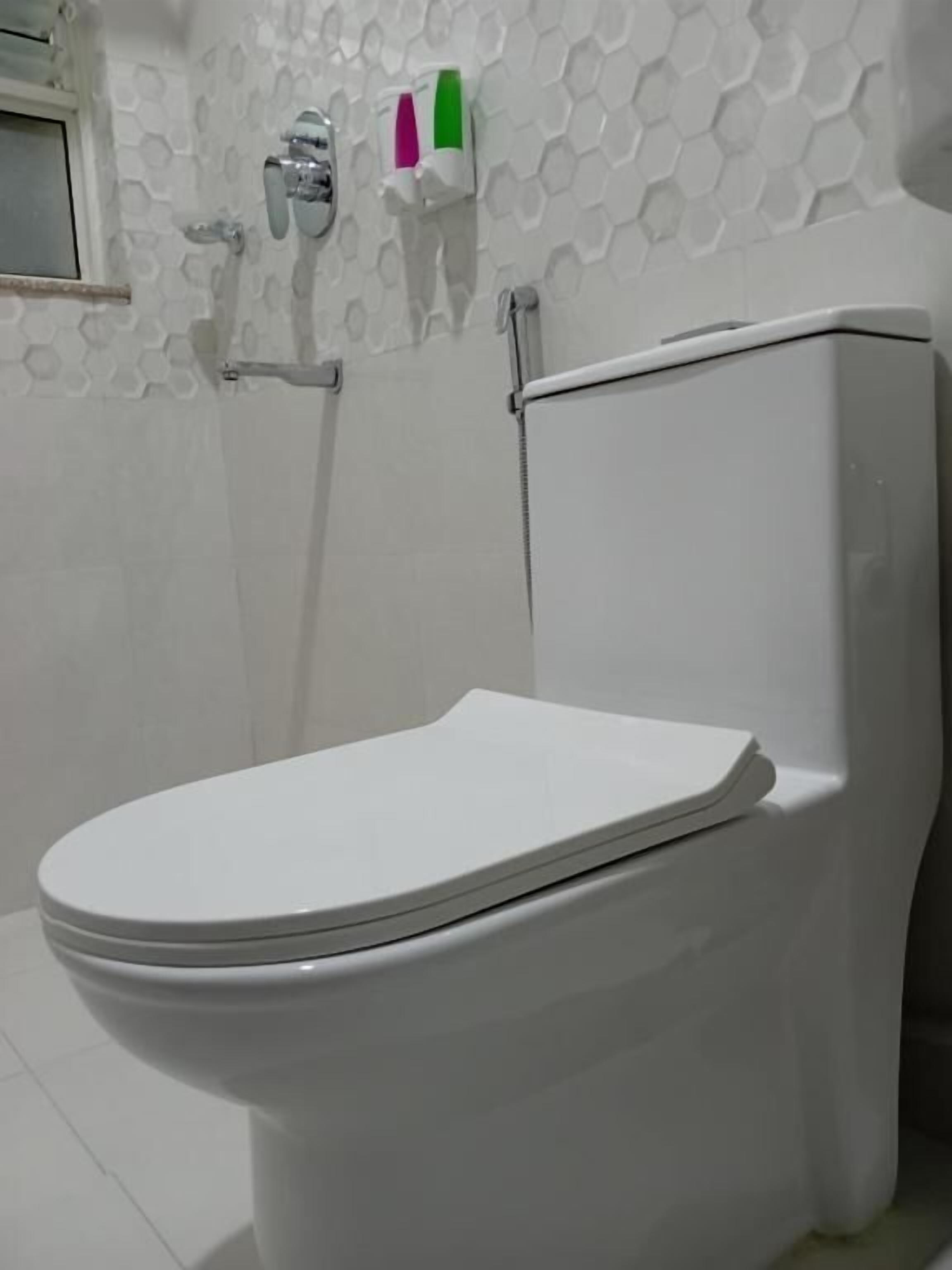A white toilet in a bathroom with a hexagonal patterned wall and a window to the left.