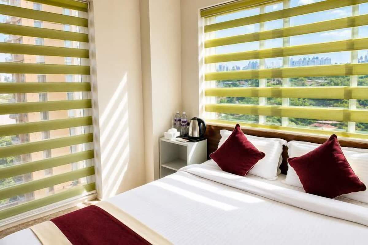 A hotel room with a bed, pillows, a nightstand, and a window with blinds.