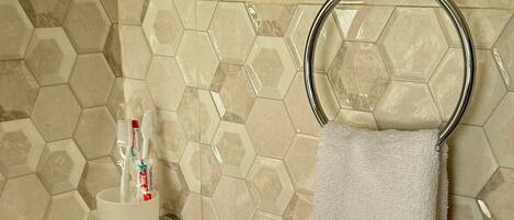 A bathroom with hexagonal tile walls, a towel ring, and a cup holder with toothbrushes.