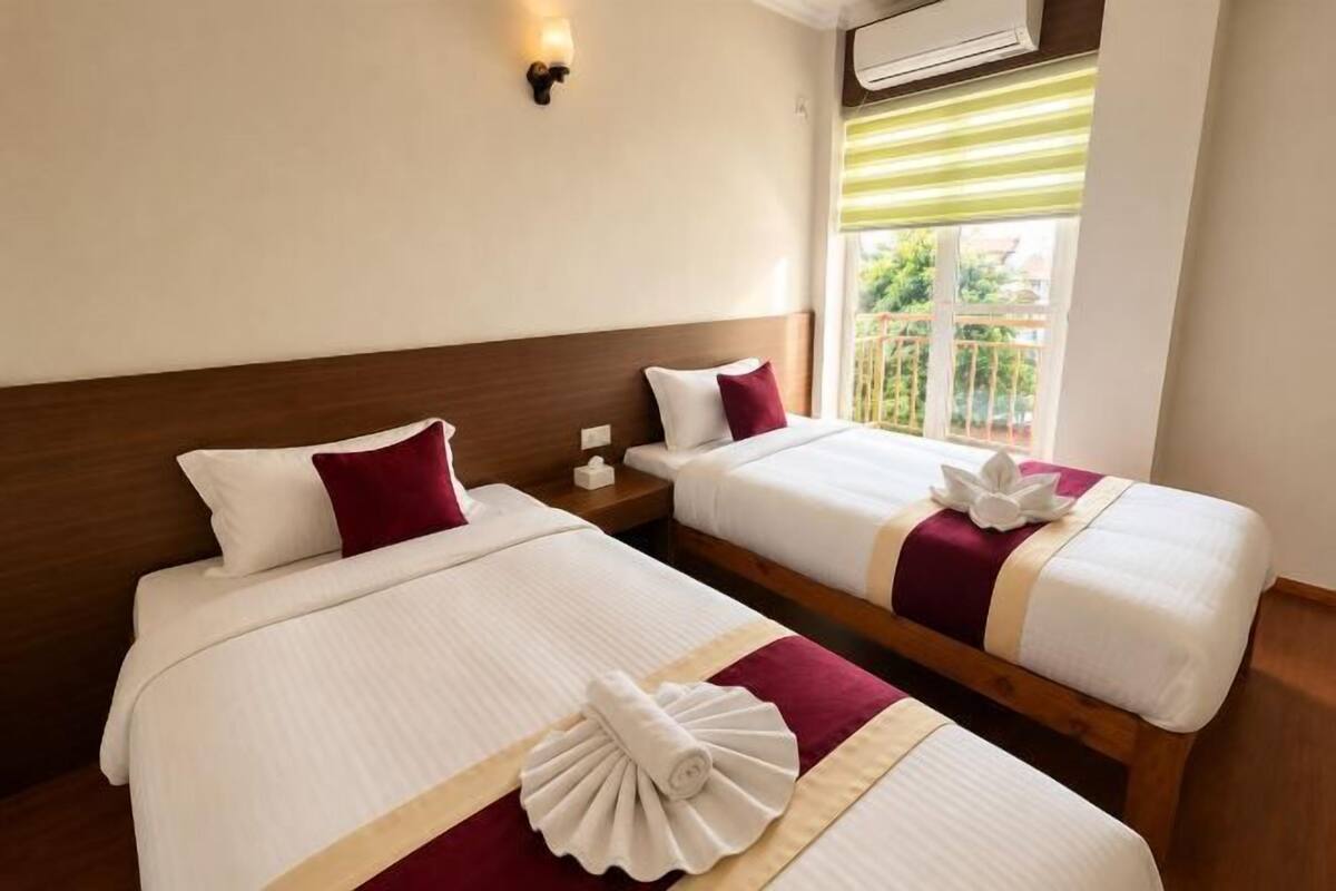 Two adjacent beds with white linens, red pillows, and decorative towels.