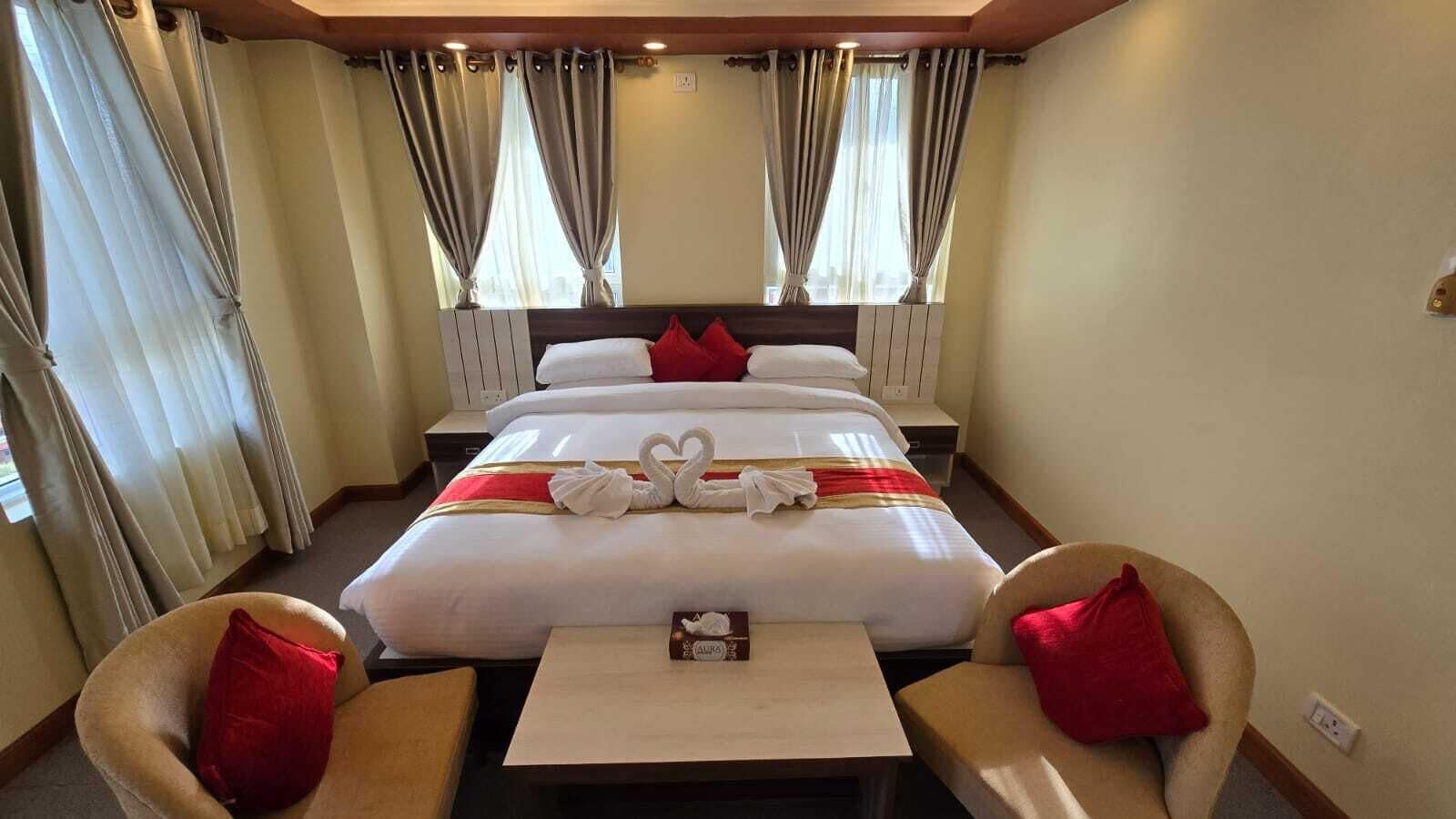 Una habitación de hotel con una cama grande, dos sillones, una mesita y cortinas.