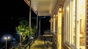 A balcony with a table and chairs, a brick wall, and a window. - Hotel Dolkha Durbar (Bhimeshwar)