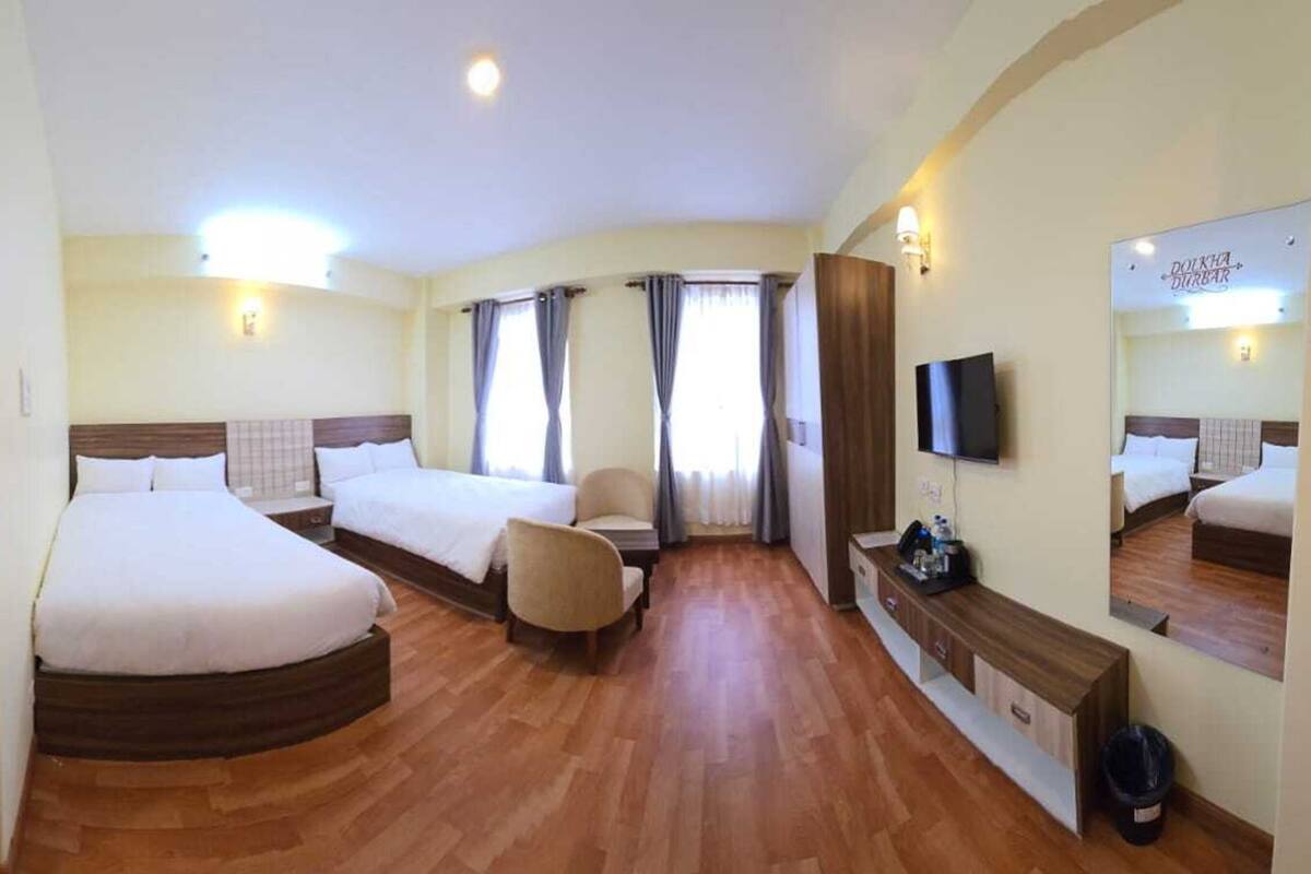 A hotel room with a large bed, a smaller bed, a sofa, a TV, and a bathroom visible through an open door.