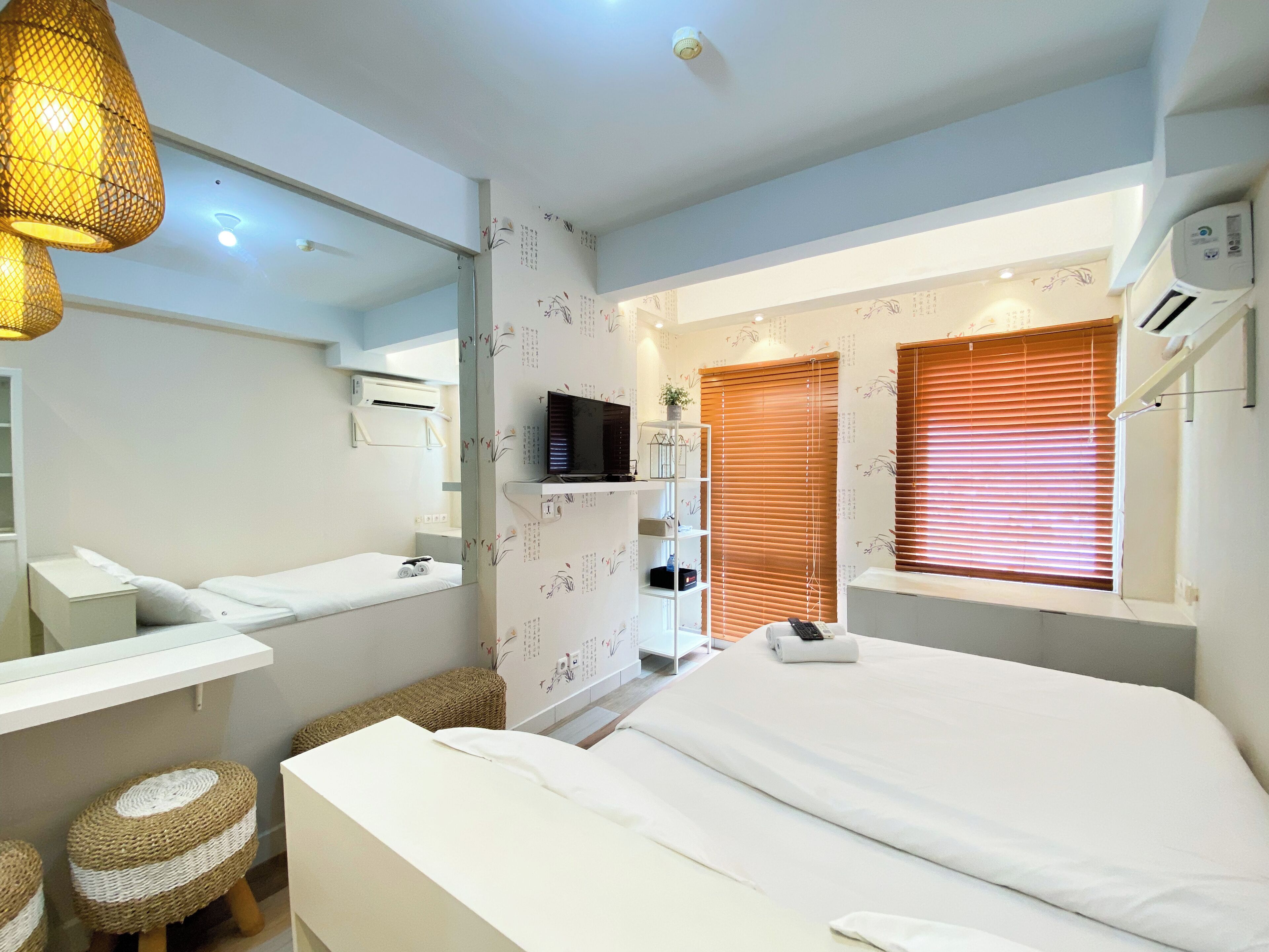 A modern hotel room with a bed, a TV, a bathroom with a mirror, and a window with blinds.