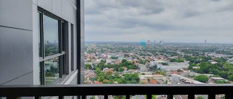 A high-rise building with a view of a cityscape, including residential and commercial buildings, and a distant view of tall skyscrapers under a cloudy sky.