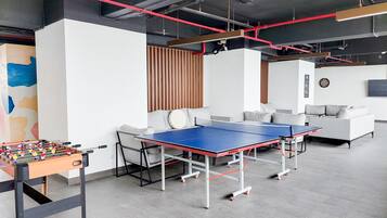A modern indoor space with a foosball table, ping pong table, and sofas.