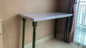 A room with a white table against a textured beige wall, green legs, and a window with a curtain. - Minimalist Studio Apartment at Springhill Terrace Residence (Jakarta)