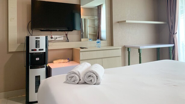 A hotel room with a bed, a TV mounted on the wall, a minibar, a mirror, and a window with curtains. - Minimalist Studio Apartment at Springhill Terrace Residence (Jakarta)