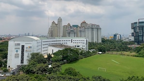 A modern building with a green roof, surrounded by lush greenery and a soccer field. - Minimalist Studio Apartment at Springhill Terrace Residence (Jakarta)