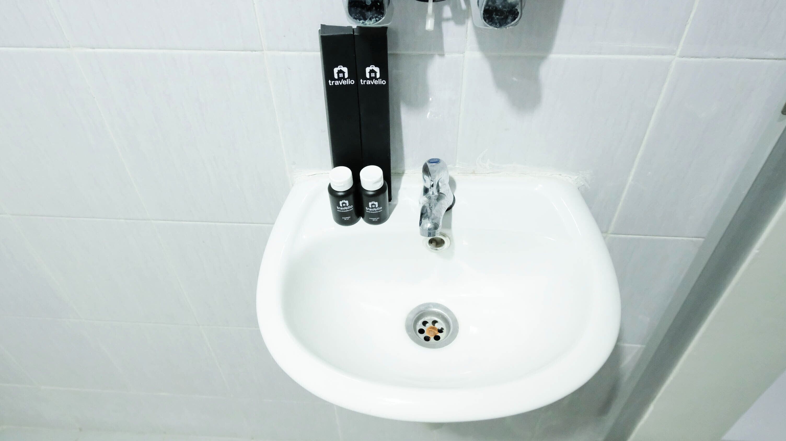 A white sink with a modern faucet and two bottles of toiletries labeled 'Travelio'.