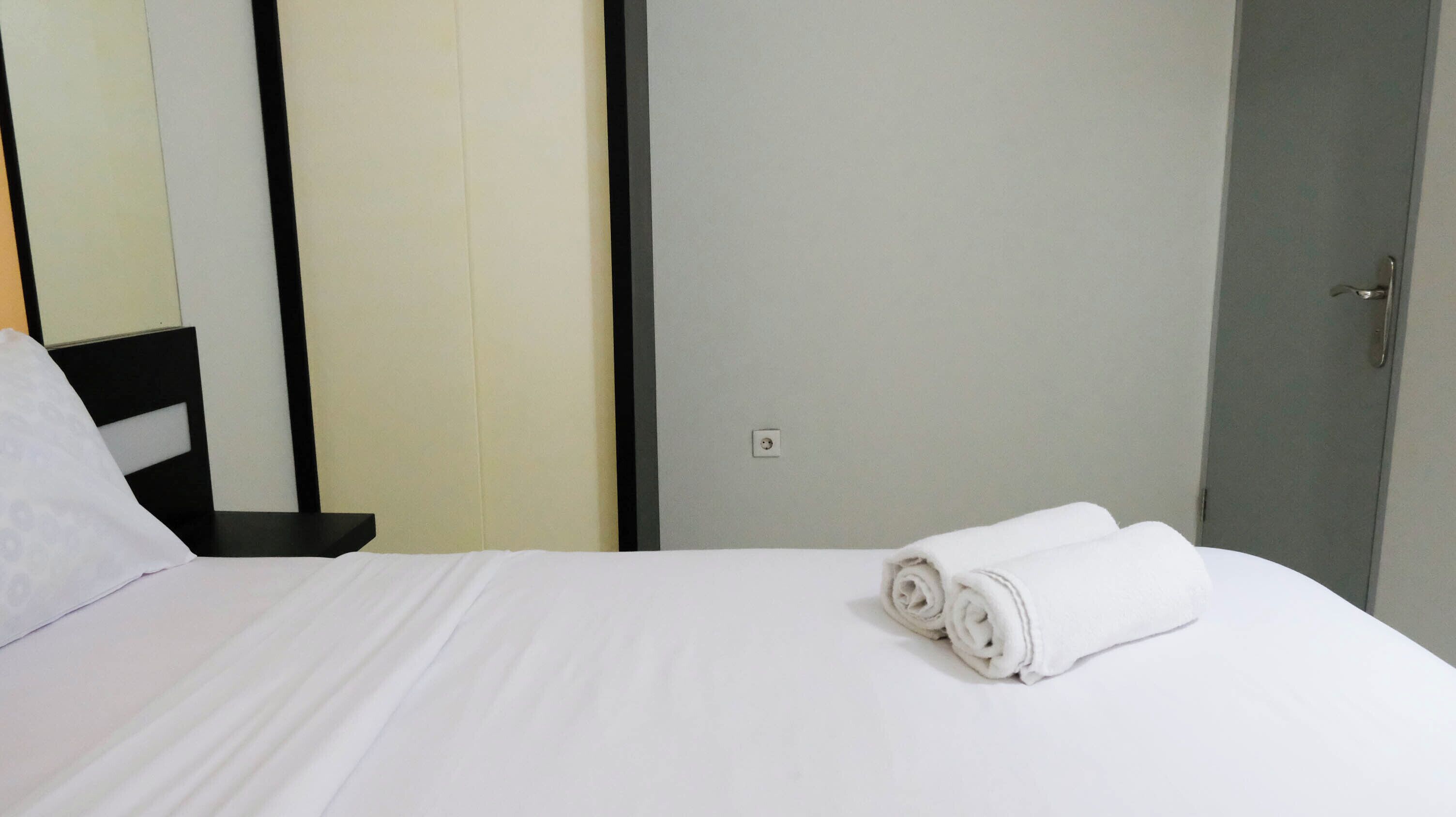 A neatly made bed with white linens and two rolled towels on it.